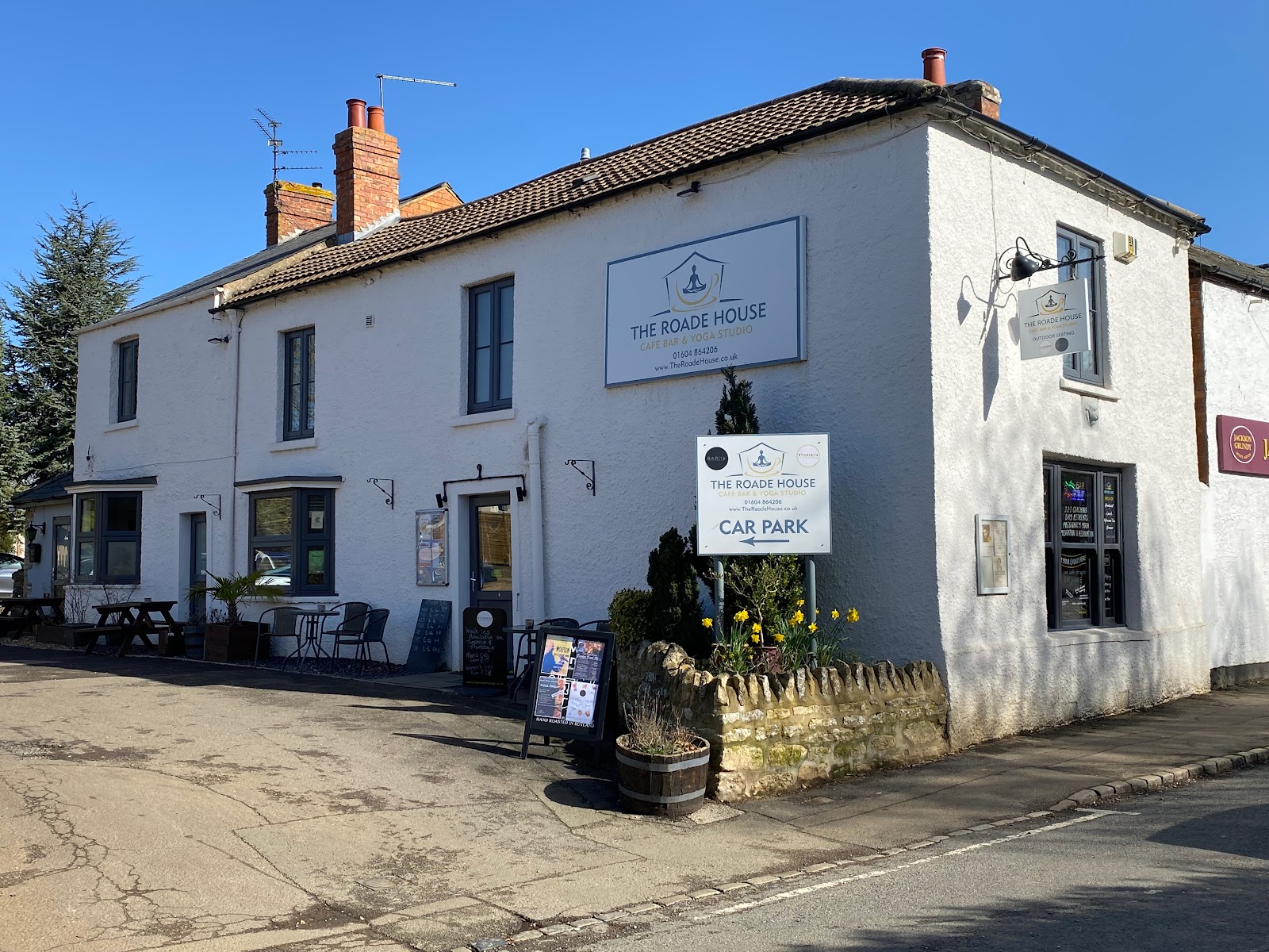 The Roade House in Roade, a white building with outdoor seating and café bar yoga studio signage.